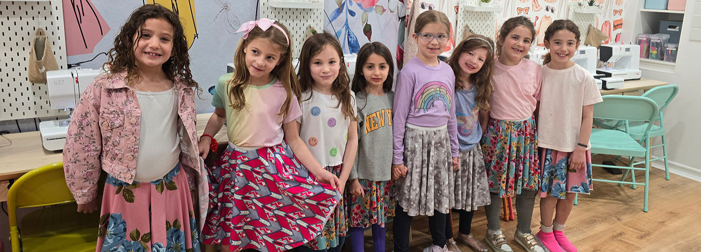 Group of young girls posing together in a classroom setting with colorful walls and furniture.
